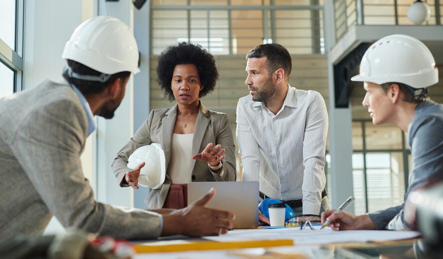 Group of diverse project managers communicating while working on blueprints at construction building.