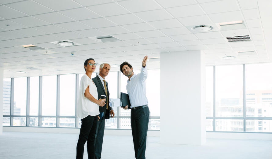 a group of men standing in a room with windows and a ceiling with white walls